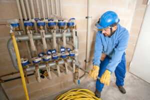 A technician in a blue helmet and gloves adjusts plumbing valves in a utility room, ensuring proper water flow within the system as part of routine maintenance.